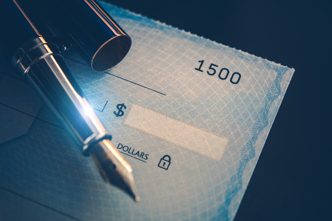 The corner of a paycheck with dollar sign on it and a fountain pen...