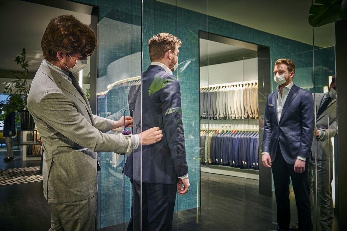 A tailor works on a suit a man inside a glass box is wearing...