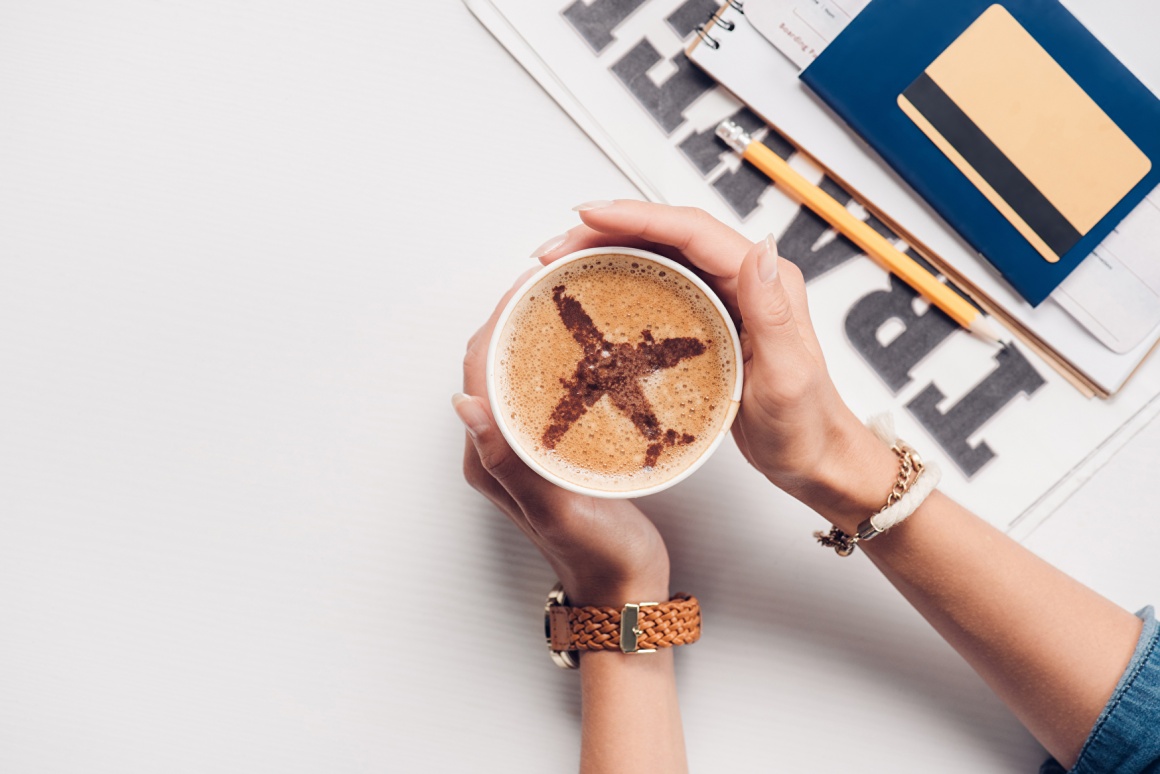 Woman holding a cup of capuccino with an airplane drawn in...