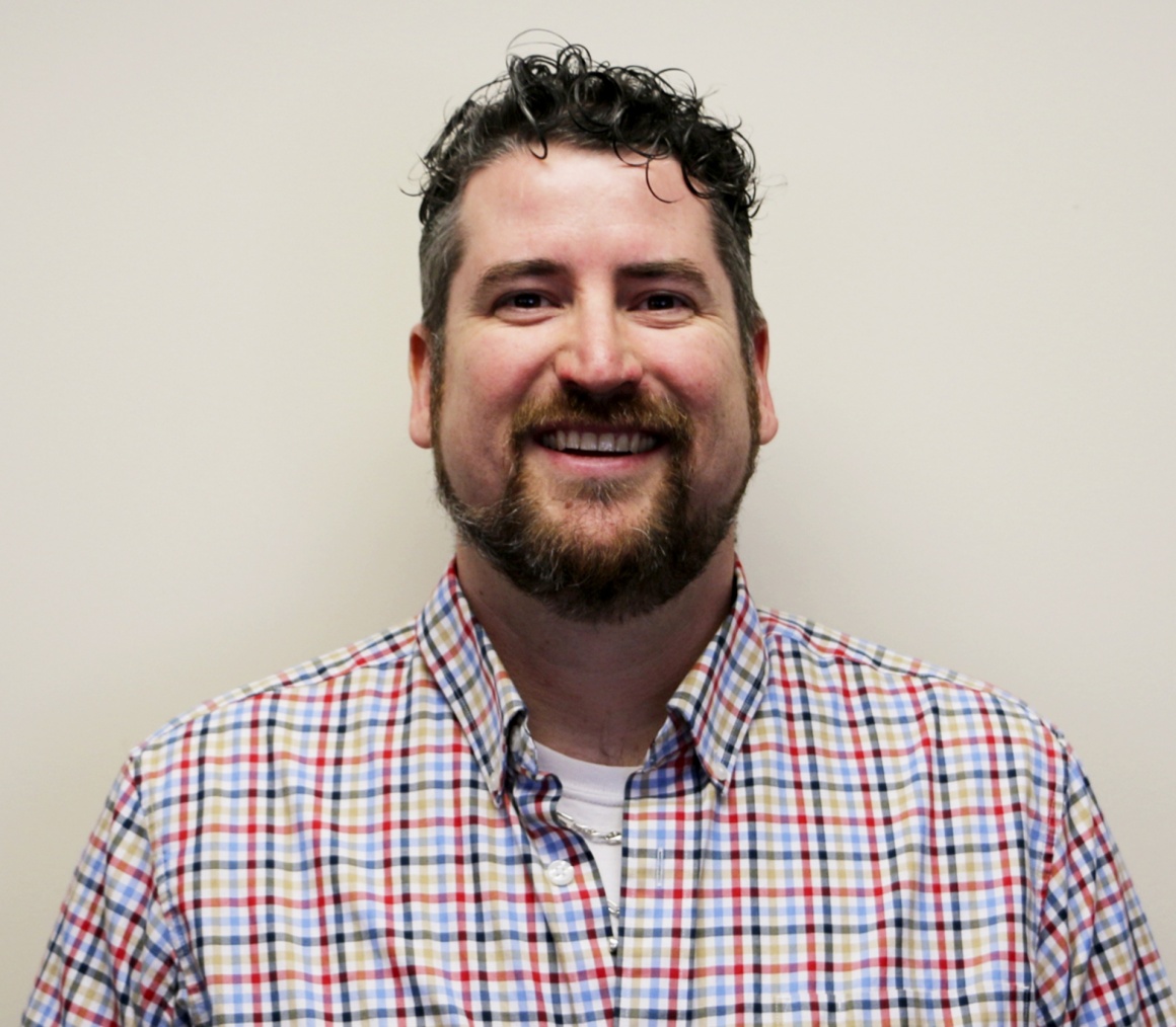 A man in a plaid shirt smiling into the camera