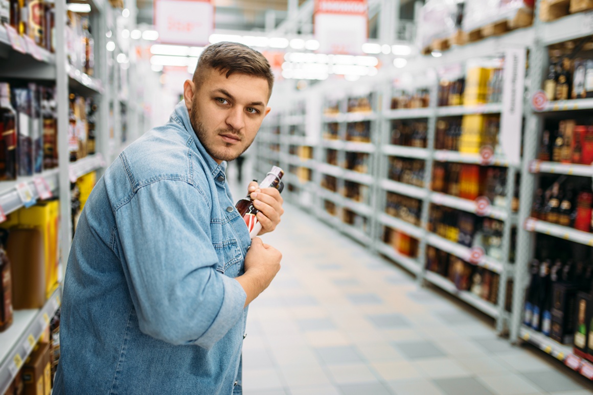 A man is sticking a bottle into his shirt in a store...