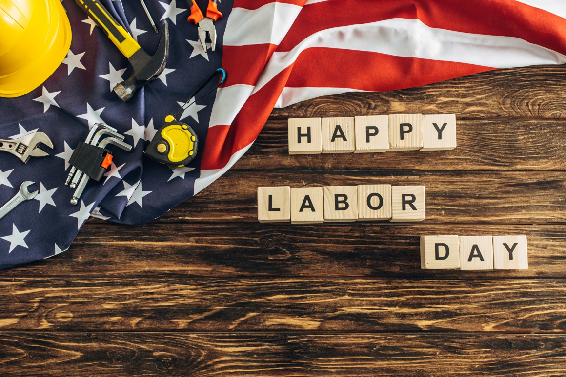 An American flag and tools lying on a wooden table with blocks spelling Happy...