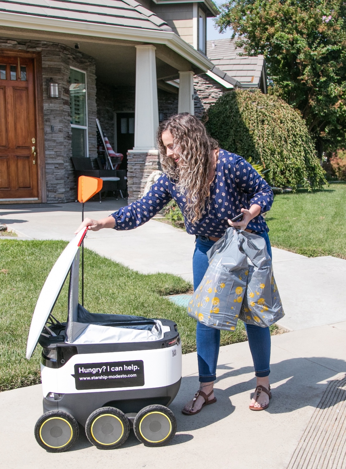 A woman is taking shopping bags from a delivery robot...