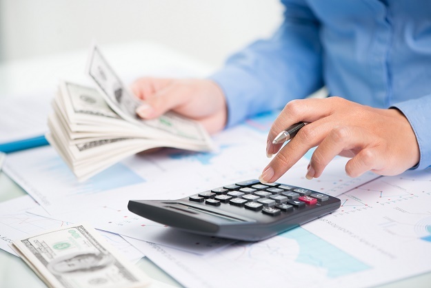 Man counts paper money with left hand while entering amounts in a calculator...