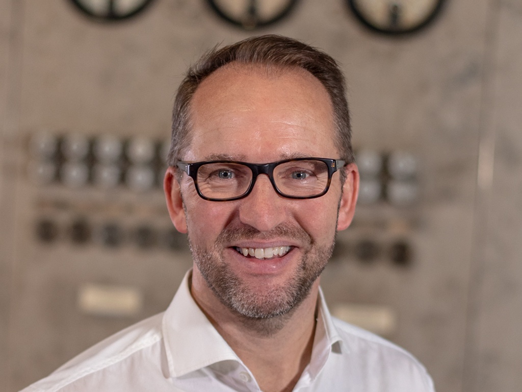 Man with glasses in a white shirt smiles at the camera...