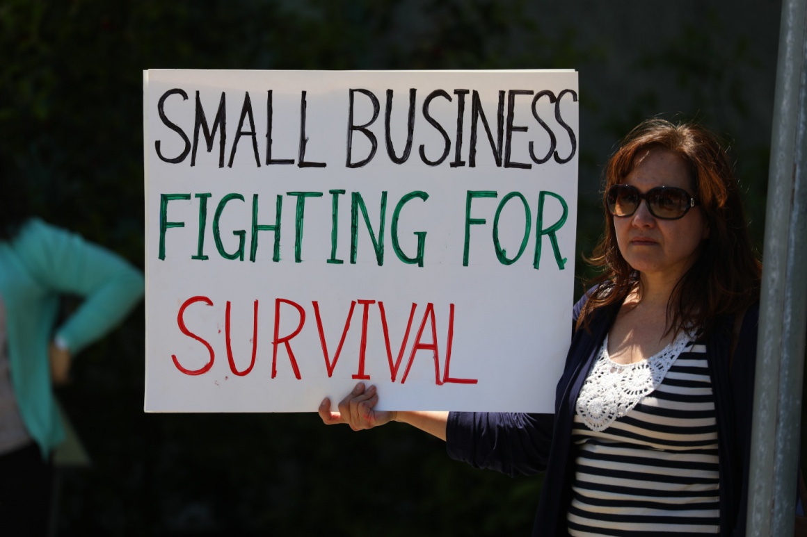 A woman holding a sign that says “small businesses fighting for survival”;...