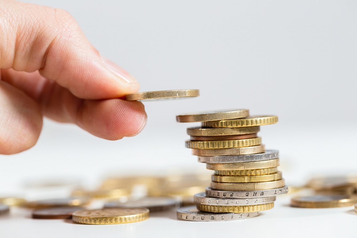 Fingers build a wobbly stack of coins