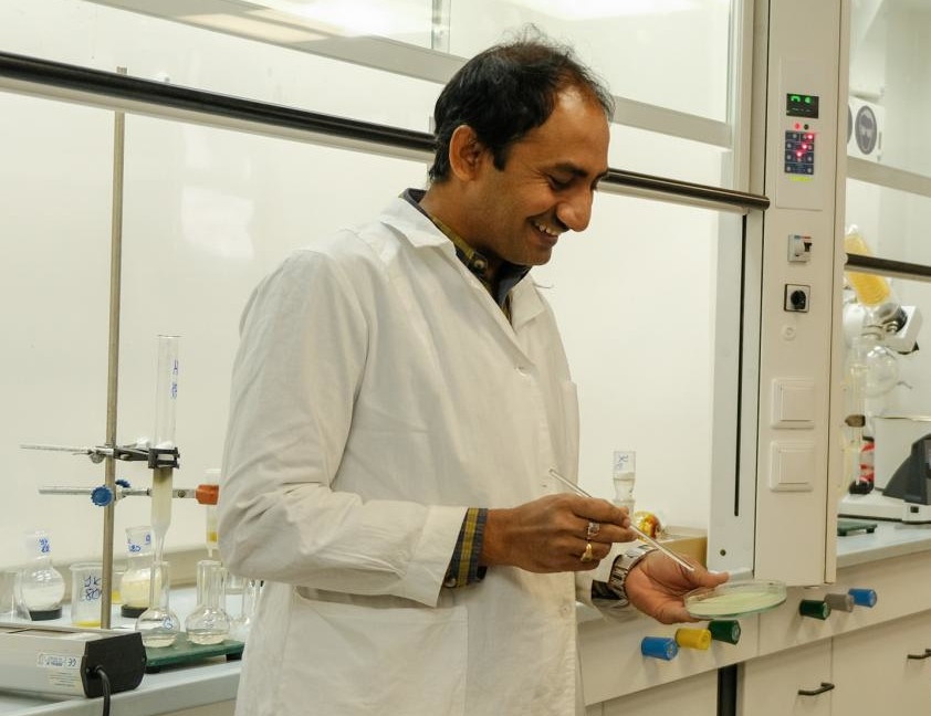 A scientist in a laboratory holding a Petri dish and a pipette...