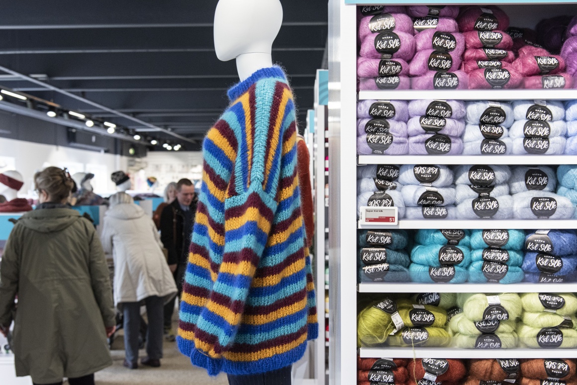 A mannequin with colorful sweater next to a shelf with wool...