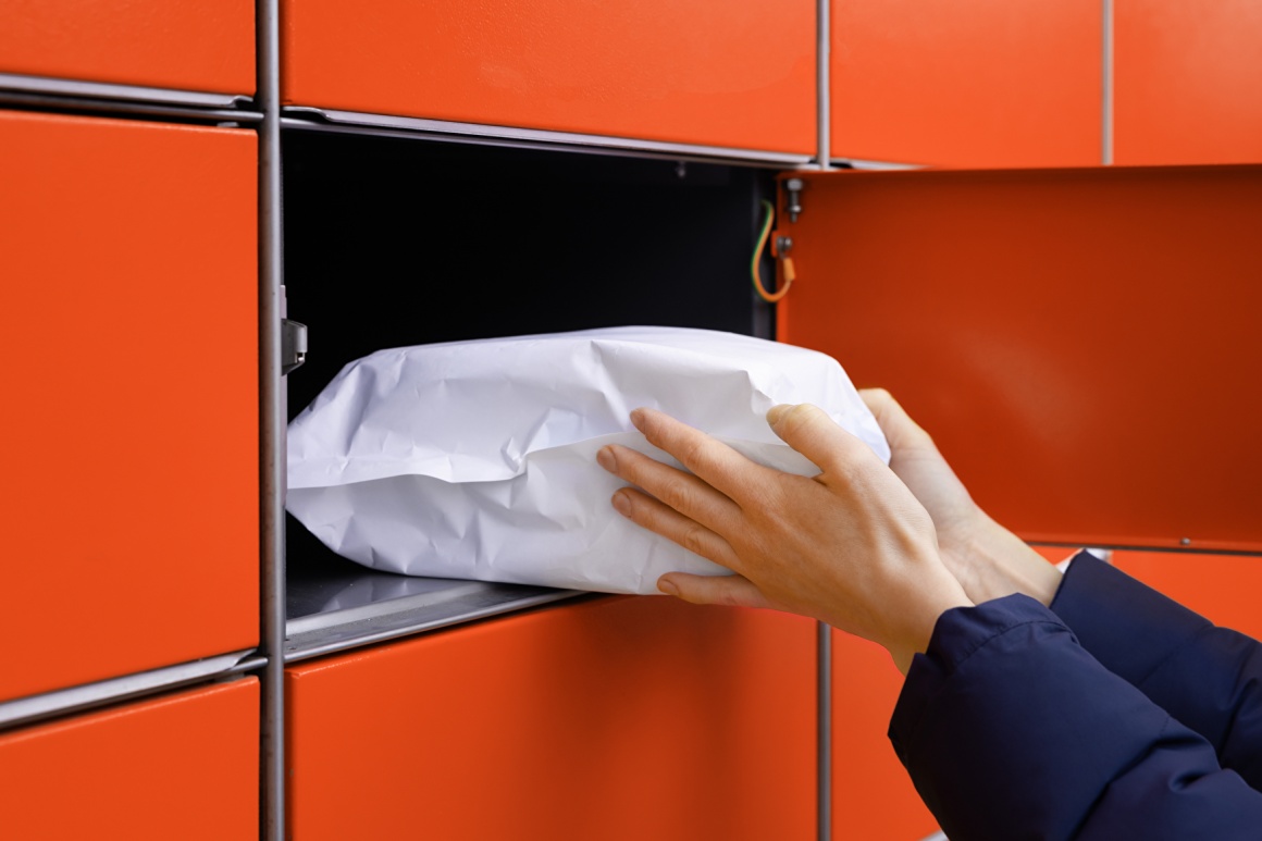 A person taking a package out of a red package lock box; copyright:...