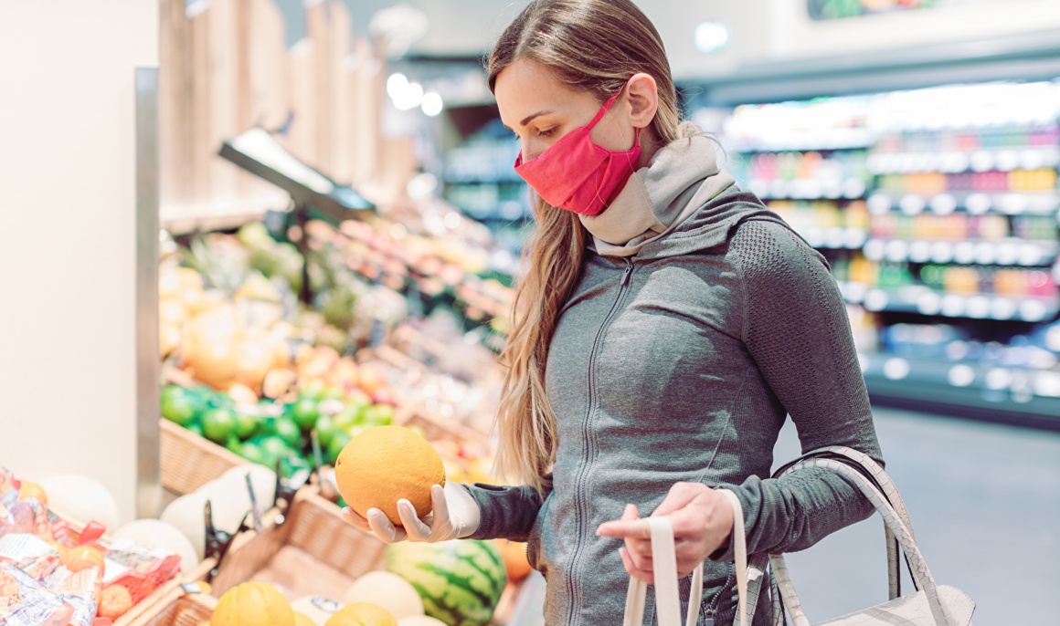 A woman is standing in a supermarket holding an orange...