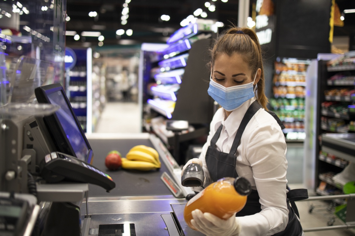 Cashier in supermarket wearing mask and gloves fully protected against corona...