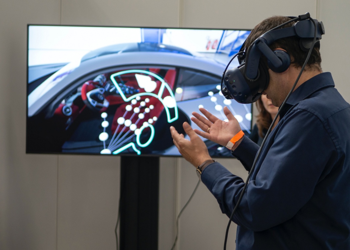 A man wearing a virtual reality headset in front of a screen looking at his...