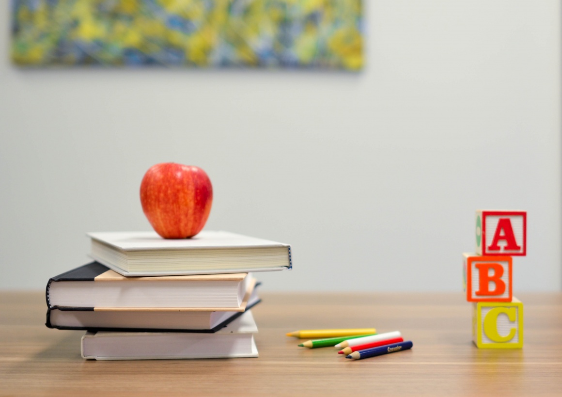 An apple lays on a pile of books next to pencils and colorful dices with letters...