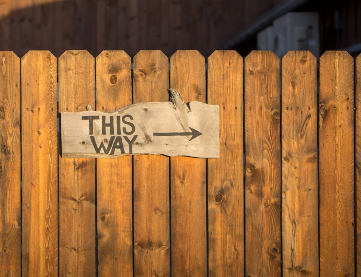 A wooden sign with an arrow on a wooden fence