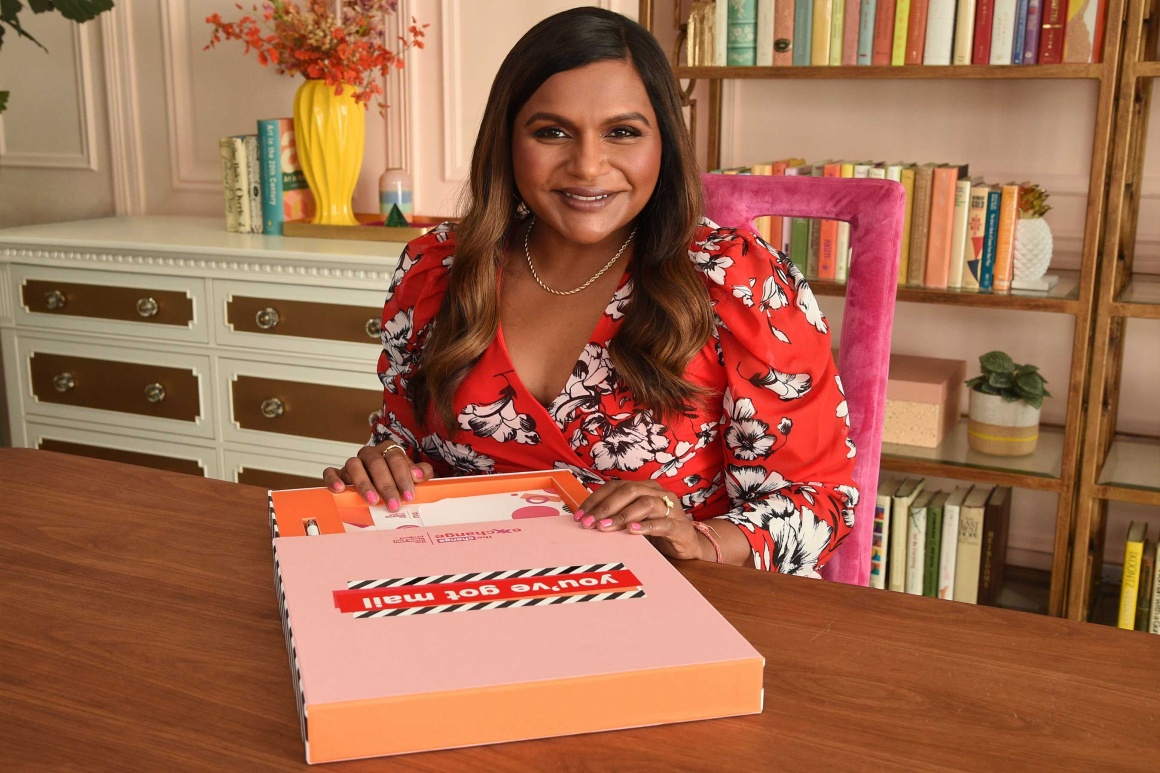 Woman wearing a colorful shirt sits in front of a box with letters and smiles...