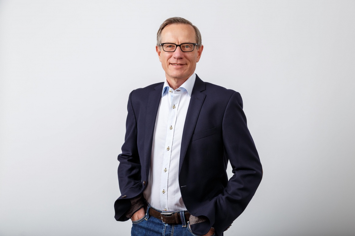 Man in black suit and with glasses smiles at the camera...