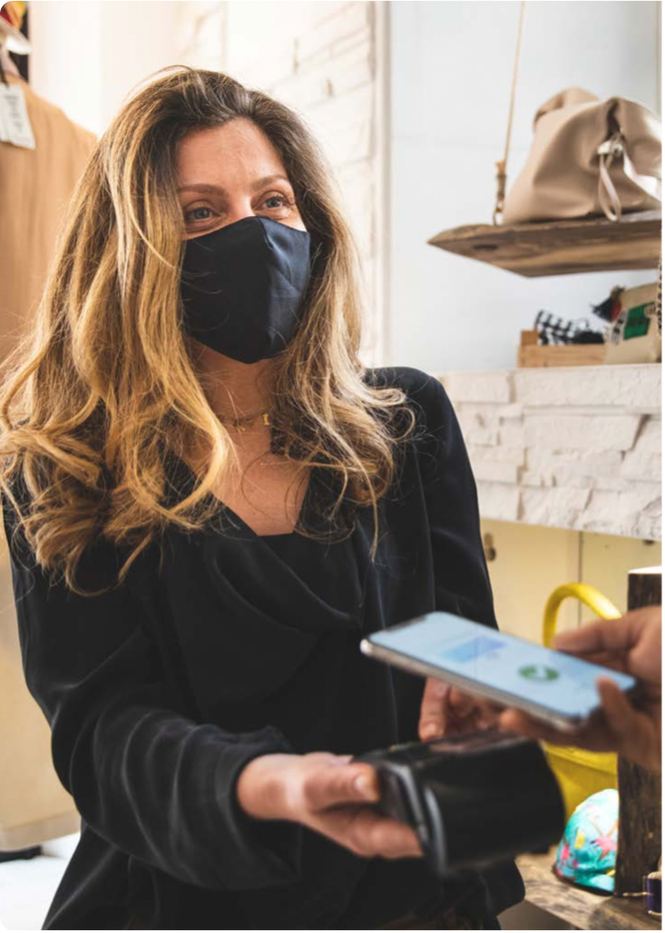 a woman holds a mobile payment terminal out to a customer with a smartphone to...