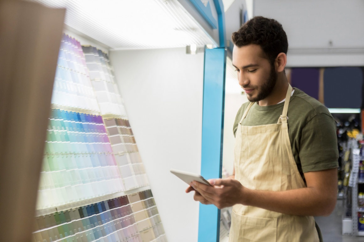 A man stands in front of a shelf full of color samples...