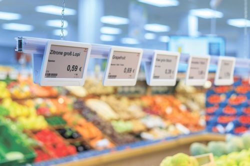 Digital price labels hang side by side above a fruit counter...