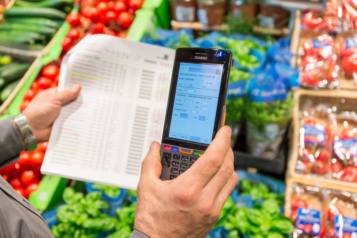 A person is standing in a vegetable department of a supermarket holding a...